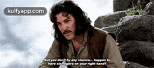 a man with long hair and a mustache is sitting on a rock talking to someone .