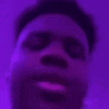 a close up of a man 's face in a purple room with a purple light behind him .