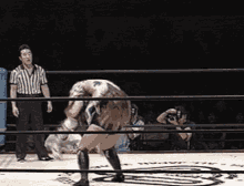 a referee stands behind a wrestling ring watching two wrestlers