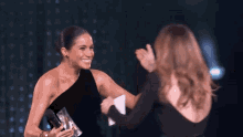 a woman in a black dress holds a microphone and talks to another woman