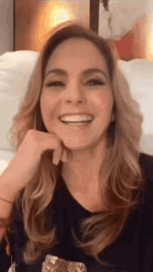 a woman with long hair is smiling with her hand under her chin