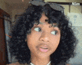 a woman with curly hair is wearing sunglasses and a pearl necklace with the word nim on the bottom