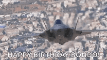 a fighter jet is flying over a city with the words `` happy birthday bondo '' written on it .
