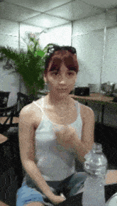 a woman in a tank top sits at a table with a bottle of water
