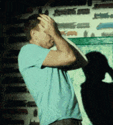 a man in a blue shirt holds his head in front of a wall with train pictures