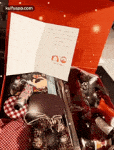 a red box filled with christmas decorations and a card on top of it .