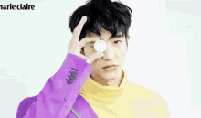 a young man in a purple jacket and yellow turtleneck is holding an egg in his hand .