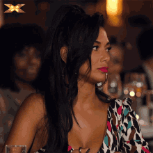 a woman with a ponytail is sitting at a table with a gold x in the background