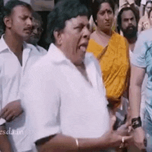a man in a white shirt is standing in a crowd of people with his tongue out .