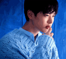 a young man wearing a blue sweater and a blue shirt is holding his finger to his mouth