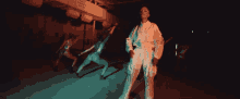 a woman in a white jumpsuit stands in front of a group of dancers