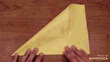 a person folding a piece of yellow paper with the words made in animotica visible