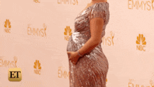a pregnant woman stands in front of a wall that says emmys on it