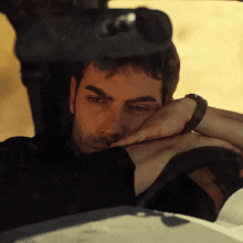 a man rests his head on the steering wheel while wearing a watch