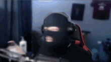 a man wearing a ski mask and headphones is sitting in a chair in front of a computer .