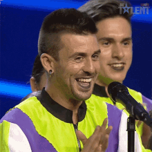 a man is smiling and clapping in front of a microphone that says talent