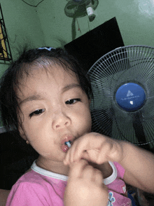 a little girl is brushing her teeth in front of a fan that says " trademark " on it