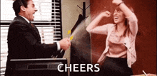 a man and a woman are sitting at a desk in front of a television and a sign that says `` cheers '' .