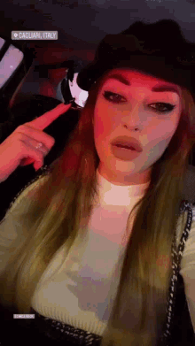 a woman wearing a hat and a sweater is sitting in a car and pointing at the camera .