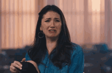 a woman in a blue denim shirt is crying while holding a pair of black shoes .