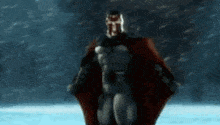 a man in a superhero costume is standing in the snow with his cape spread out .