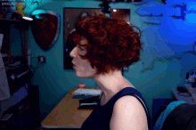 a woman with red hair is sitting at a desk in front of a blue wall that says grim.ost.boot.org