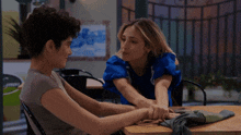 a woman in a blue shirt is sitting at a table with her head on her arms .