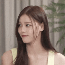 a close up of a woman with long hair wearing a yellow tank top and looking at the camera .