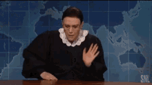 a man in a judge 's robe is sitting at a desk .