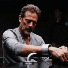 a man with a beard is sitting at a table with his hands tied up .