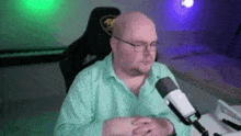 a bald man wearing glasses is sitting in front of a microphone in a room .