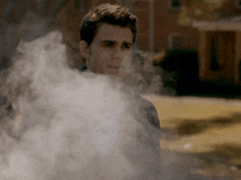 a man is surrounded by smoke and looks at the camera