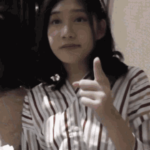 a woman wearing a striped shirt gives a thumbs up