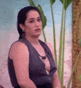 a woman in a very revealing top is sitting in front of a palm tree and looking at the camera .