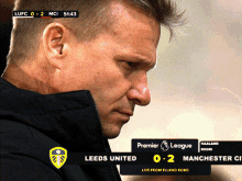 a man stands in front of a scoreboard which says premier league