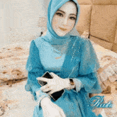 a woman wearing a blue dress and a hijab holds a cell phone in her hand