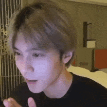 a young man with blonde hair is making a funny face while sitting on a bed in a room .