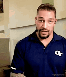 a man with a beard is wearing a blue shirt with a g on it .
