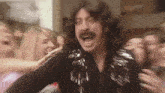 a man with a mustache is standing in front of a crowd of people and screaming .