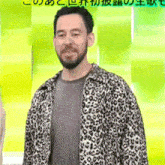 a man with a beard and a leopard print jacket is standing in front of a green wall .