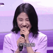 a woman in a purple shirt is smiling and holding a microphone with korean writing on it