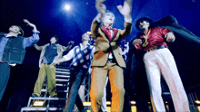 a group of men are standing on a stage with their arms in the air and one has a necklace with the letter b on it