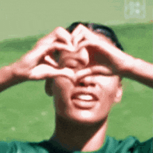 a person is making a heart shape with their hands over their eyes .