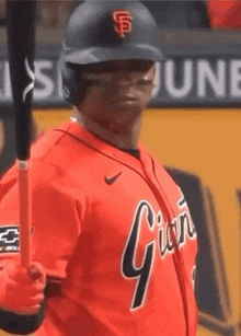 a baseball player is holding a bat and wearing an orange jersey that says giants