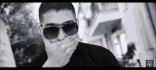 a black and white photo of a man wearing sunglasses covering his mouth