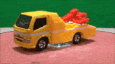 a yellow toy tow truck is sitting on a red surface .