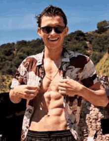 a shirtless man wearing sunglasses is holding a glass of water .
