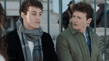 two young men are standing next to each other and one has a scarf around his neck .