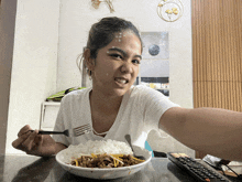a woman sitting at a table with a bowl of food and a remote