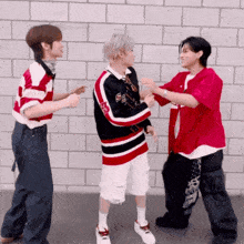 three men are dancing in front of a brick wall and one of them is wearing a red shirt with the letter r on it